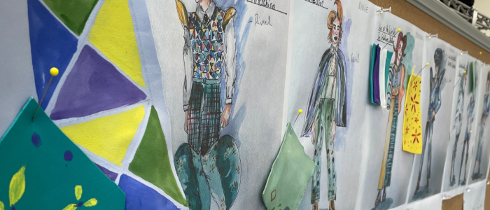 A row of costume renderings for characters in Connecticut Rep's War of the Worlds (Fall 2023) pinned to a board, along with green and yellow swatches and patterns for construction.