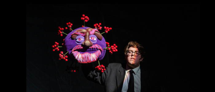 Puppeteer Jerry Harney for Connecticut Rep's production of War of the Worlds (Fall 2023) holding a spherical purple puppet with bushy eyebrows and beard with clusters of red nodes jutting out of it.