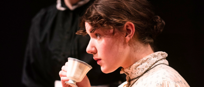 Emilie (Morgan Hrymack) hesitantly sipping tea as she attempts to make sense of her new environment in Connecticut Rep's production of The Moors (Fall 2024).