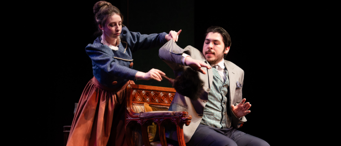 An ambitious maid dusts under the arm of a serious gentleman in the 2024 production of A Doctor's Dilemma.