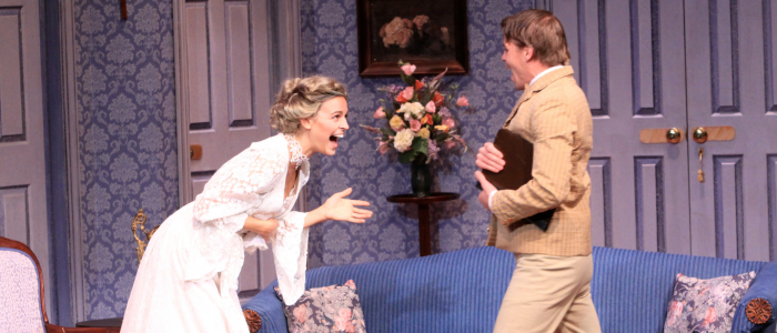 Connecticut Repertory Theatre's A Flea in Her Ear (2011) with one actor in a white dress smiling and laughing with another actor in a brown suit against a blue styled set with a bouquet of flowers in the background.
