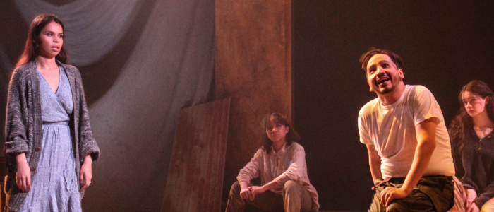 A young woman in a flowing blue dress l listens to a young man in t-shirt and jeans, sitting on a stool, in the CRT production of Seven Spots on the Sun.