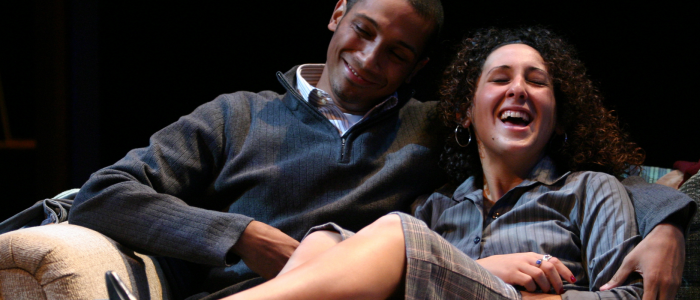 A young couple cuddle up on the sofa, laughing in the 2005 production of Stop Kiss.