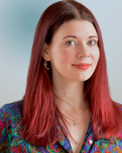 Portrait of Abbie Golec, a white woman with long vibrant red hair, wearing a colorful top, and smiling at the camera