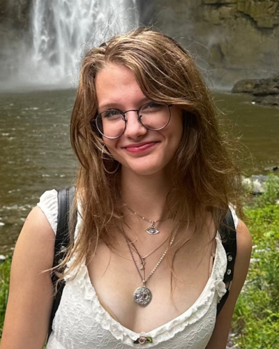 Portrait of Alfi Free, a white college student standing in front of a waterfall, smiling.