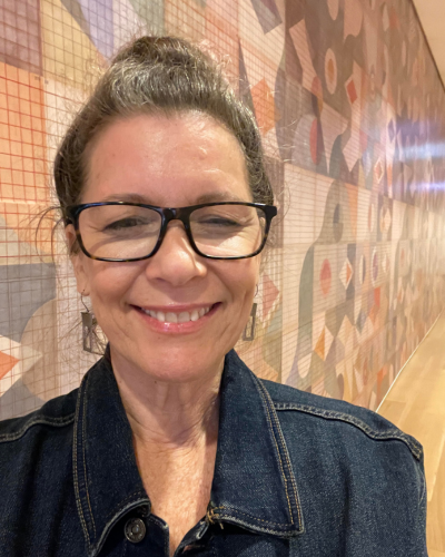Portrait of a woman wearing glasses and a jean jacket, smiling at camera.