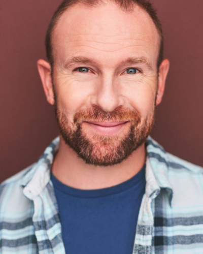Portrait of Brad Fraser, a white man with short cropped hair and facial hair, smile broadly at the camera