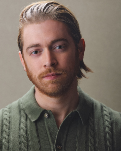 Portrait of Chris Martin, a white graduate student with slicked-back strawberry blonde hair wearing a green knit shirt.