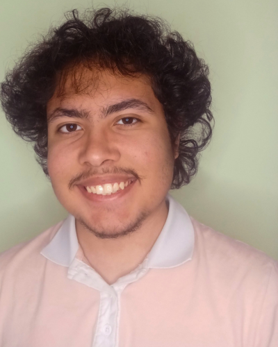 Portrait of Christopher Cazarin, an hispanic college student with dark hair and moustache, wearing a pink shirt.