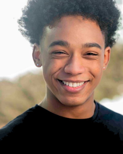 Portrait of Djanne Martinez, a black college student with a huge smile, wearing a dark t-shirt.