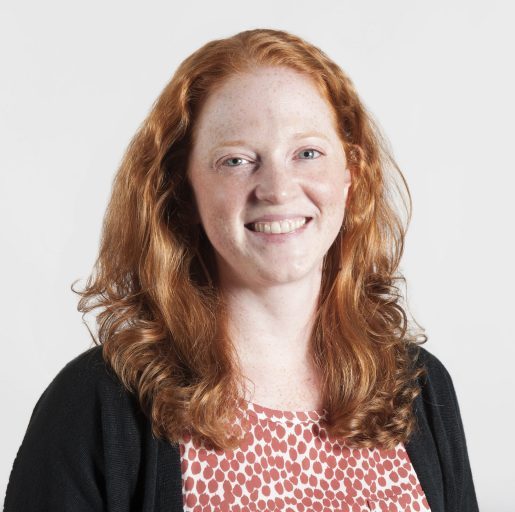 Portrait of a white woman with long red hair, smiling at the camera