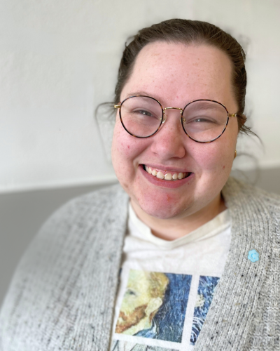 Portrait of Emma Sowards, a white graduate student with her dark hair pullled back, wearing a grey cardigan and round glasses.