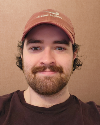 Portrait of Ethan Morgan a student with dark hair, beard and mustache, wearing an orange baseball cap