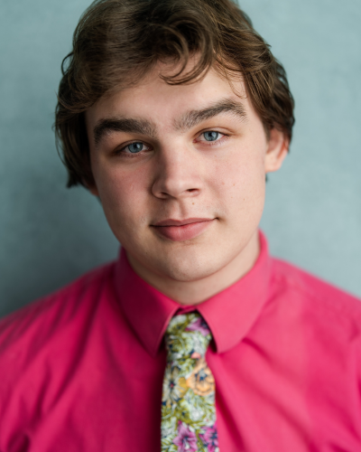 Portrait of an undergraduate student with brown hair and blue eyes, wearing a fuchsia colored button-down and a colorful tie.