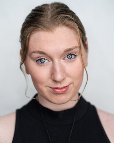 Portrait of an undergraduate student with blue eyes, wearing a black sleeveless top, with her hair pulled back.