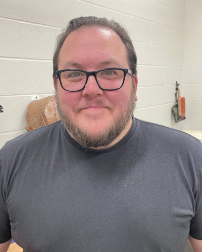 Portrait of a person with black glasses and a salt & pepper beard, wearing a grey tee shirt