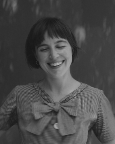 Black and white portrait of Harley Walker, a young woman with short hair and a big smile, wearing a dress with a big bow.