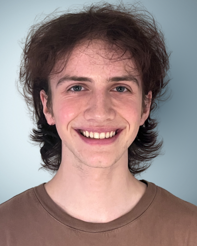 Portrait of Ian Rothauser, a college student with wavy brown hair, a big smile, and brown t-shirt.