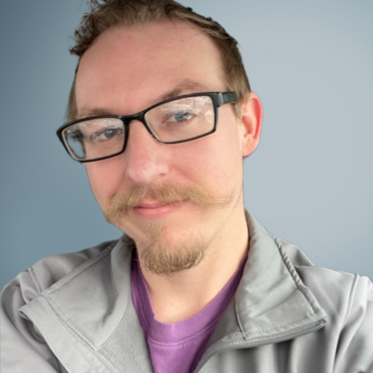 Portrait of a person wearing glasses, donning a bespoke mustache and purple t-shirt.
