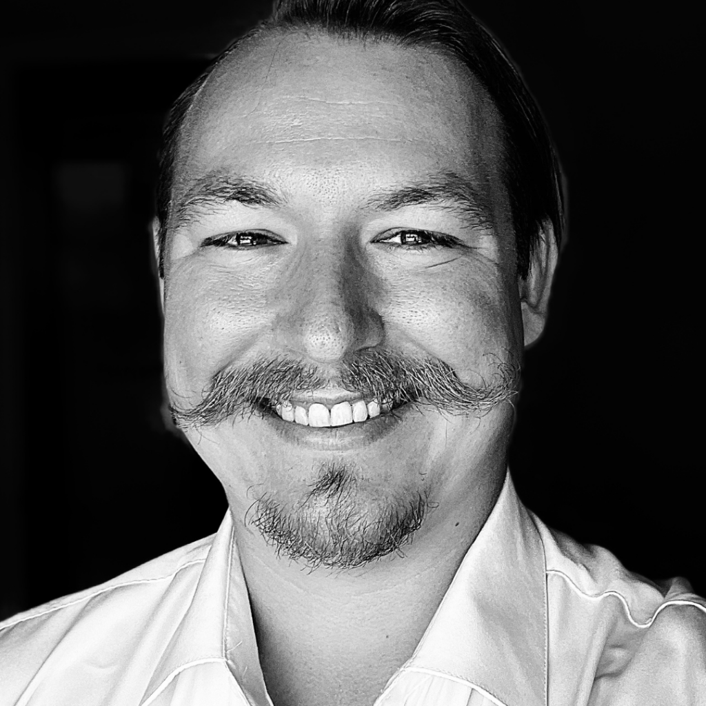 Black and white portrait of a smiling faculty/staff member with a mustache and goatee
