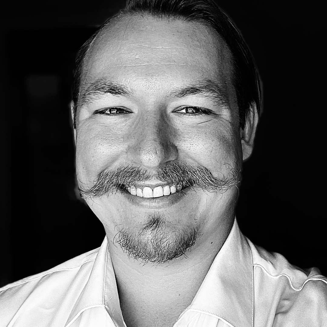 Black and white portrait of a smiling faculty/staff member with a mustache and goatee