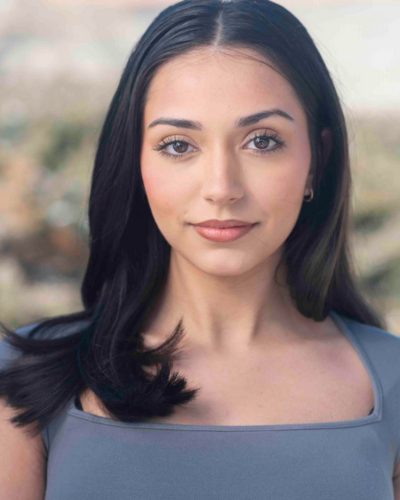 Portrait of Lia Crosby, college student with long black straight hair, and big dark eyes, wearing a grey-blue top with a square neckline.