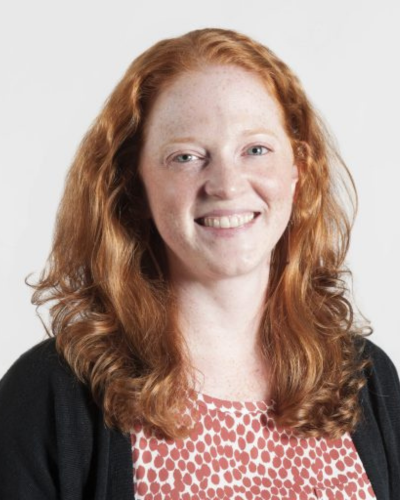 Portrait of a white woman with long red hair, smiling at the camera