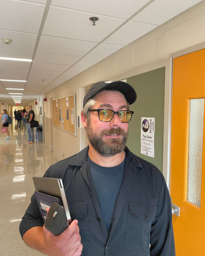 Portrait of a man with full beard & dark glasses, wearing a black baseball cap.
