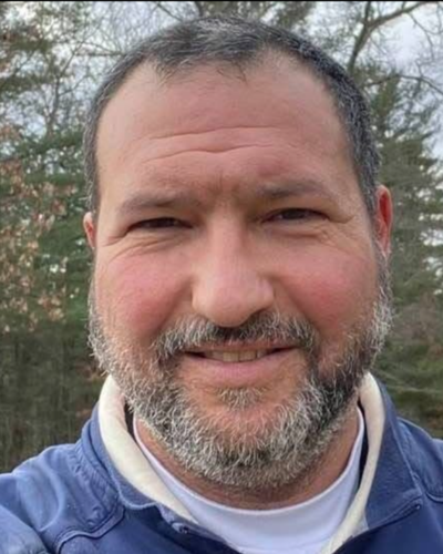 Portrait of a white man with facial hair, wearing a blue denim shirt