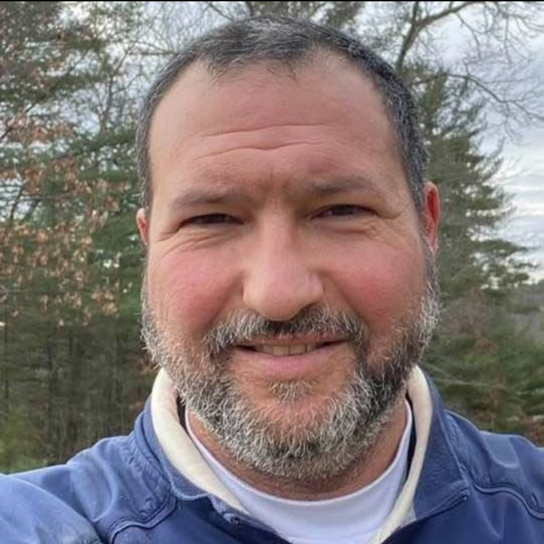 Portrait of a white man with facial hair, wearing a blue denim shirt