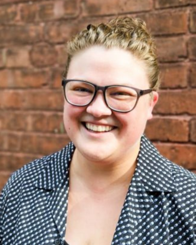 Portrait of a friendly, smiling person with black glasses, wearing a black and white polka-dotted shirt.