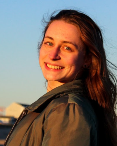 Portrait of Phoebe Thomas, a white woman with long dark hair, wearning a leather jacket.