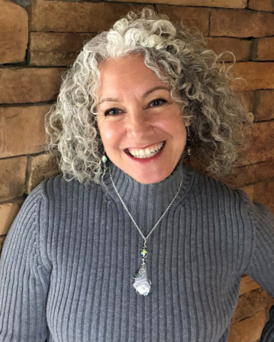 Portrait of a smiling white woman with curly greying hair and a huge smile.