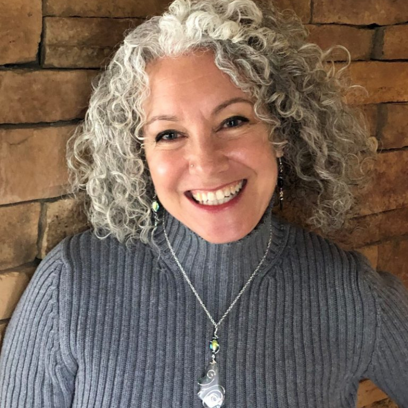 Portrait of a smiling white woman with curly greying hair and a huge smile.