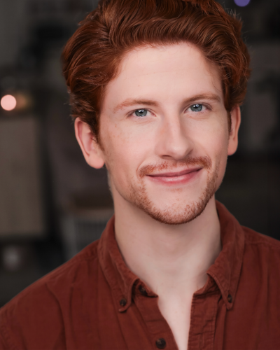 Portrait of Zachary Russell, a white graduate student with red hair and slight facial hair, smiling at the camera.
