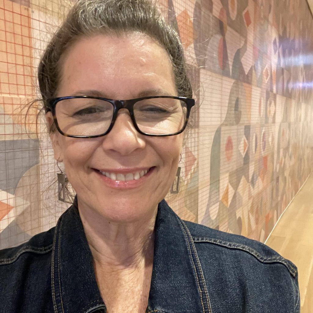 Portrait of a woman wearing glasses and a jean jacket, smiling at camera.