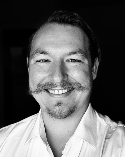 Black and white portrait of a smiling faculty/staff member with a mustache and goatee