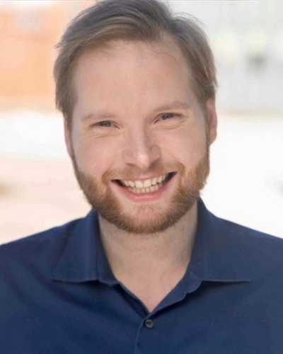 Portrait of a white graduate student with a big smile and strawberry blond facial hair.