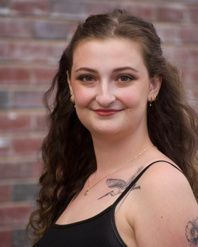 Portrait of Emma Laura Schreiber, a college student standing in front of a brick wall, smiling