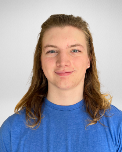Portrait of a smiling student with long brown hair, wearing a blue t-shirt.