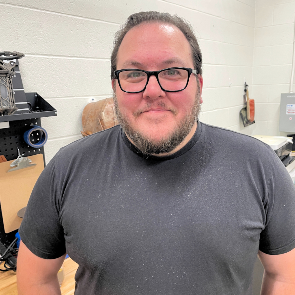 Portrait of a person with black glasses and a salt & papper beard, wearing a grey tee shirt
