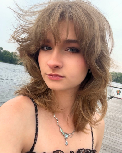 Portrait of a student with wavy brown hair, on a dock with water in the background