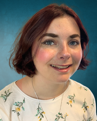 Portrait of Caelyn Dorsey, a young white woman with dark hair and a big smile