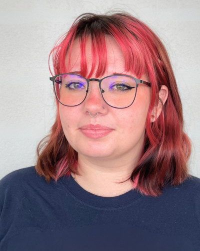 Portrait of a college student with dark pink hair, wearing a navy blue sweatshirt.