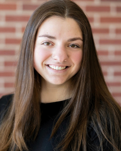 Portrait of a smiling undergraduate with long dark, straight hair, wearing a black top.