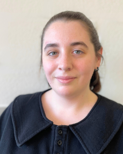 Portrait of a white undergraduate student with their hair in a ponytail, wearing a black top with a big collar.