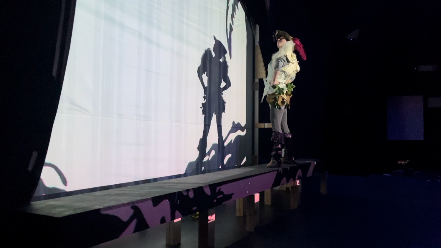 The view from backstage as we see the actor playing Pan create the shadow seen by the audience