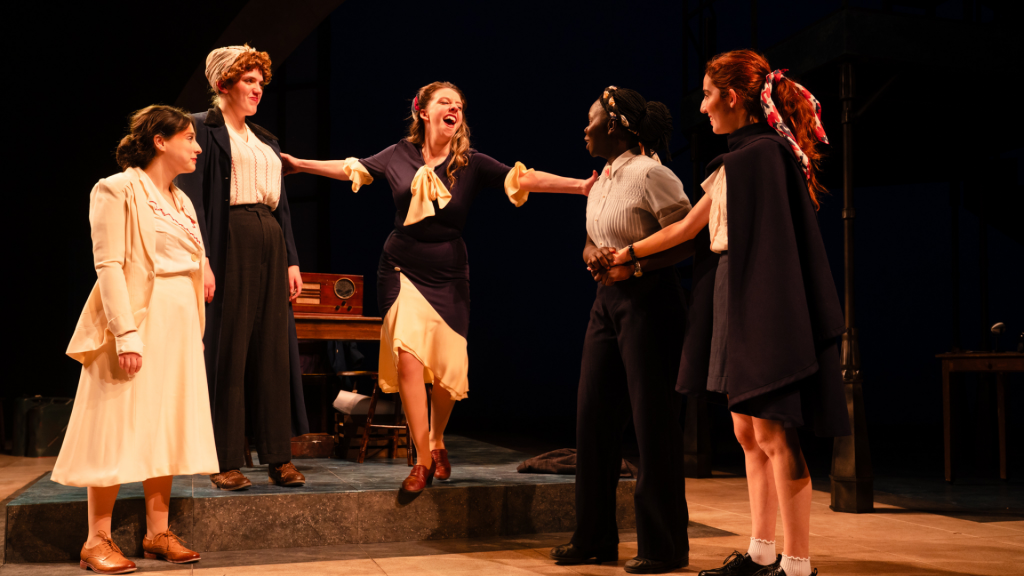 Five woman dreessed in 1940's clothing gather to celebrate a victory.