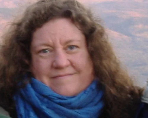 Portrait of a heavy set white woman with long, light brown curly hair, wearing a blue scarf and black jacket