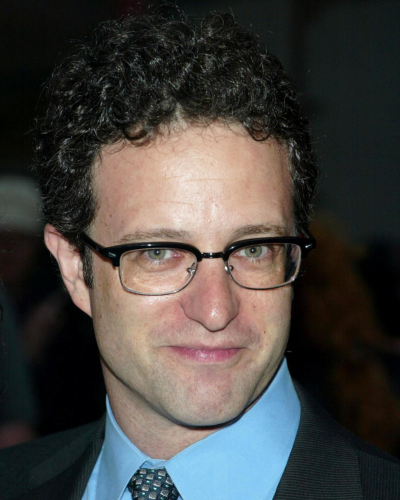 Portrait of a white man with dark curly hair and black glasses.